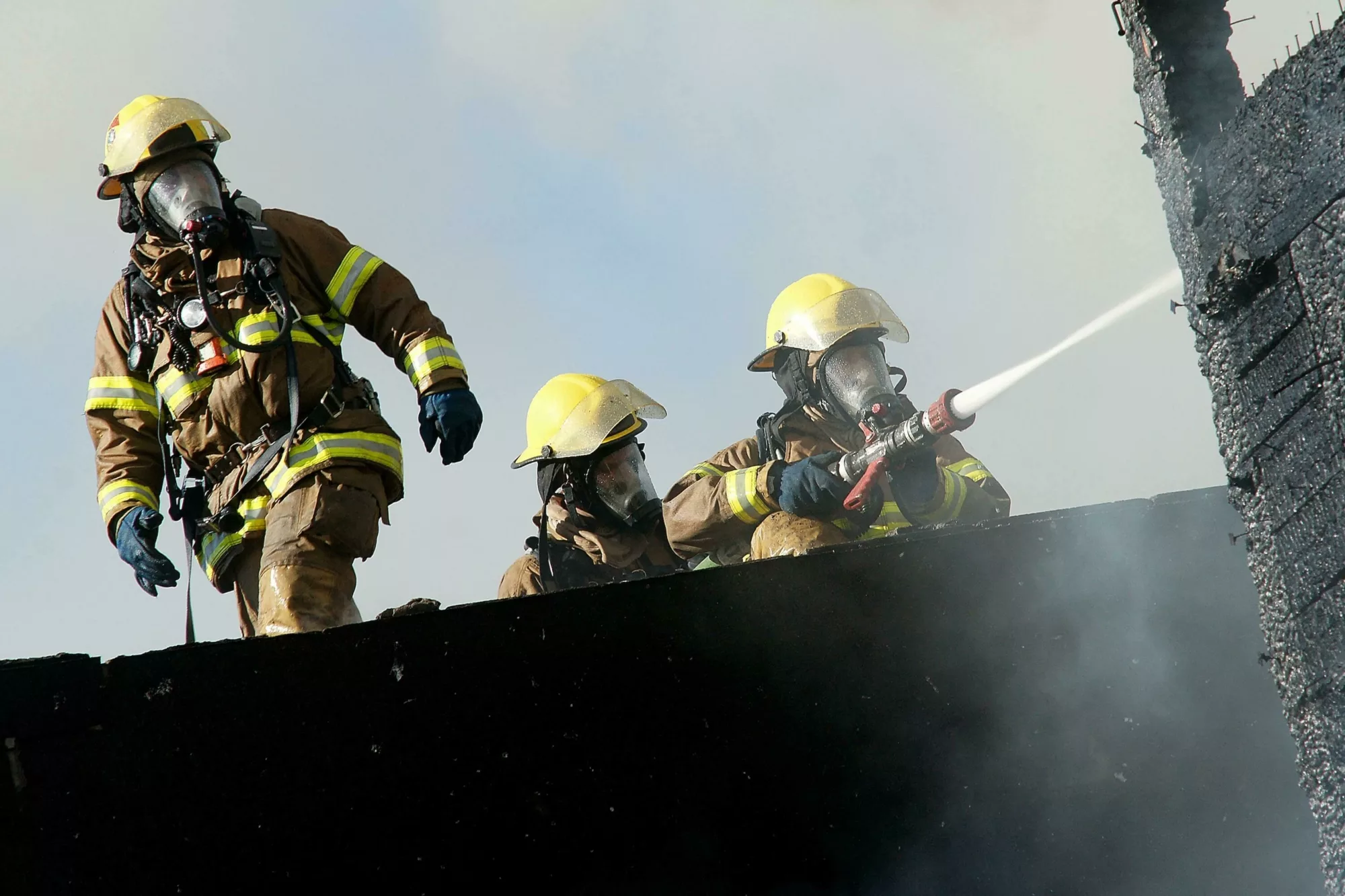 Three firefighters working together to prevent a fire using a hose.
