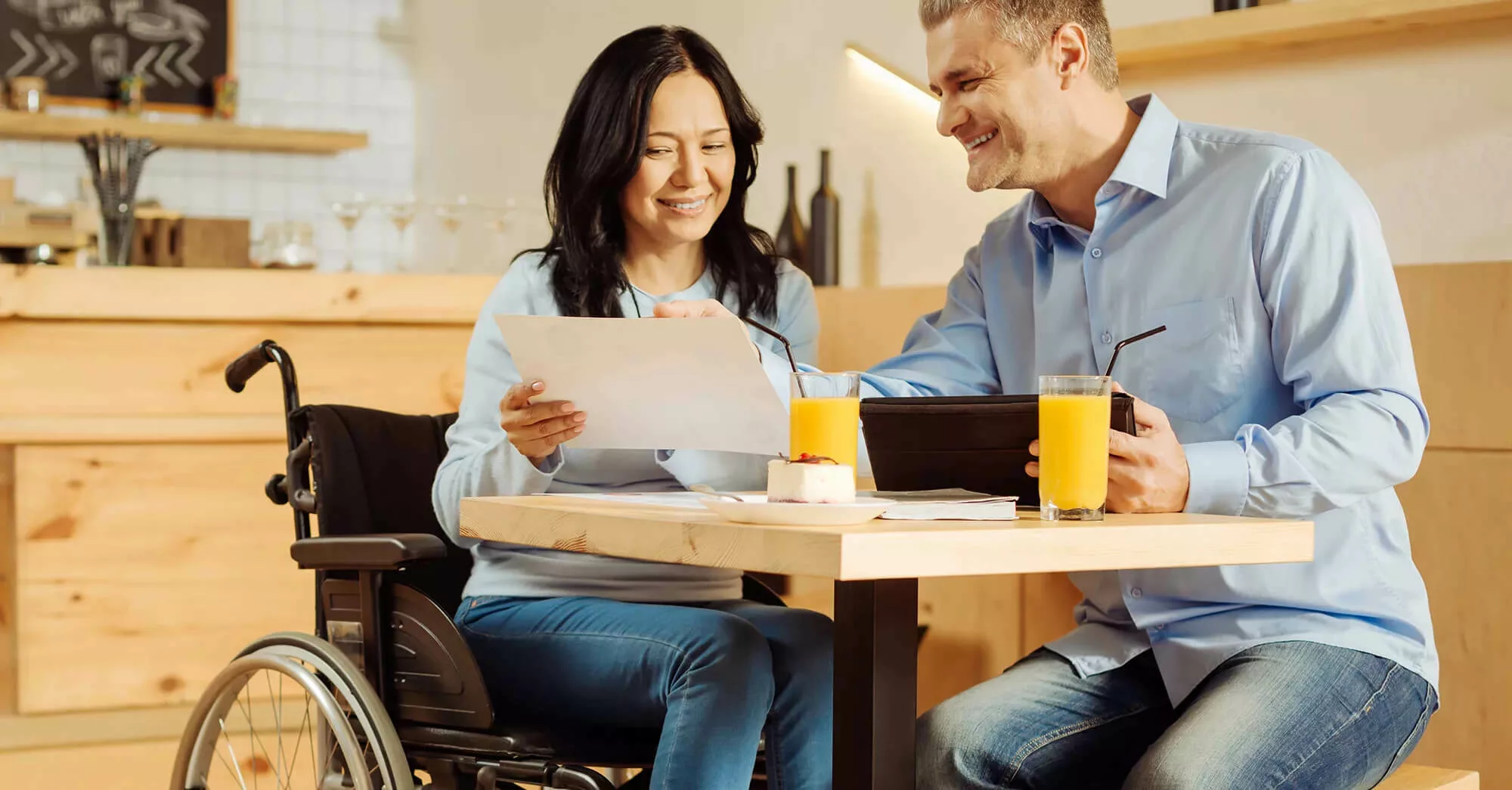 Two smiling individuals, one in a wheelchair, at a dining table discussing information together.